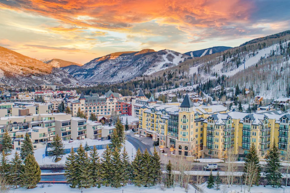 Aerial view of Vail, Colorado in winter with multi-story buildings in foregorund and snowy mountains in background.